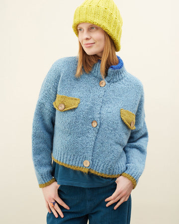 model wearing slightly cropped light blue cardigan with olive green patch pockets and trim