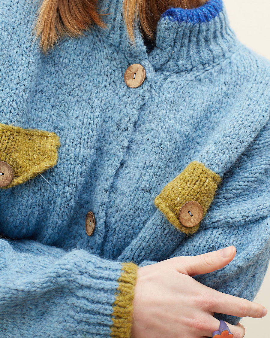 up close of model wearing slightly cropped light blue cardigan with olive green patch pockets and trim