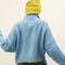 back view of model wearing slightly cropped light blue cardigan with olive green patch pockets and trim