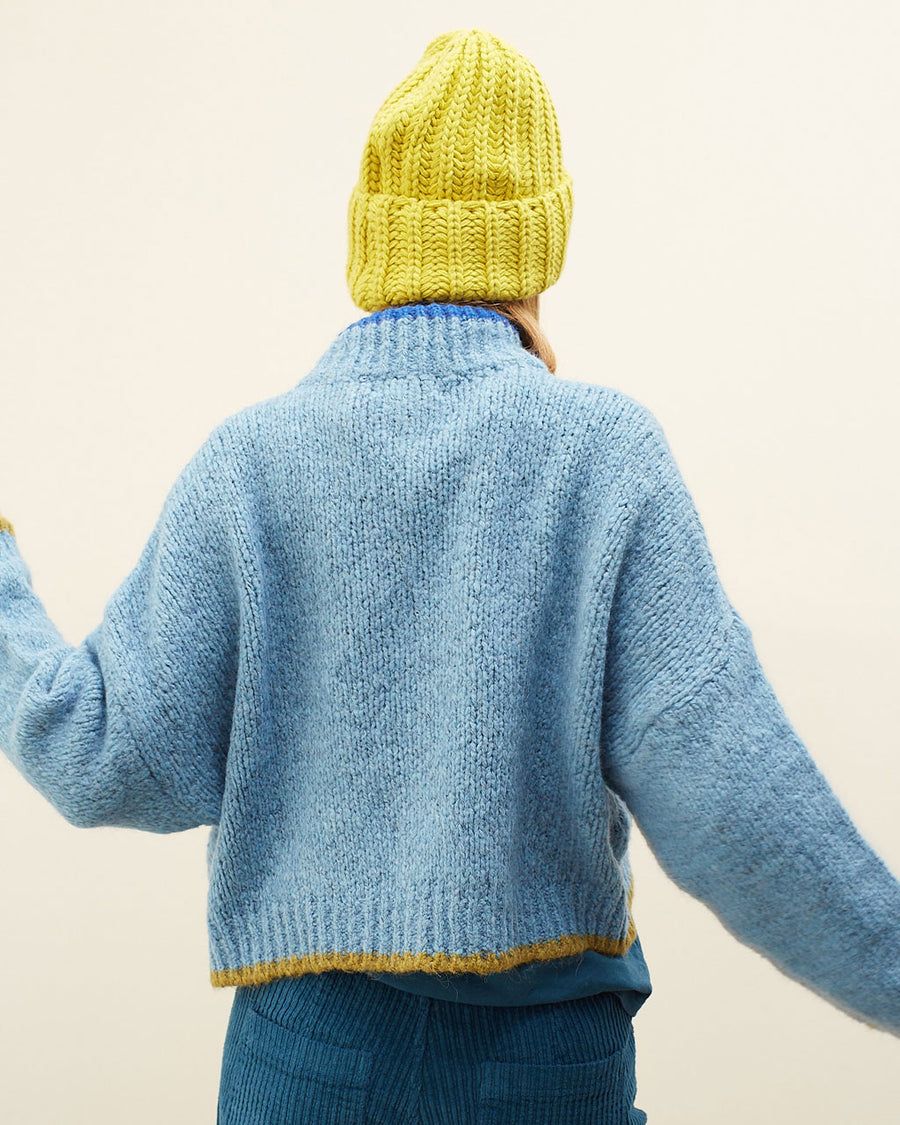 back view of model wearing slightly cropped light blue cardigan with olive green patch pockets and trim