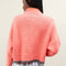 back view of model wearing slightly cropped coral cardigan with grey patch pockets and trim