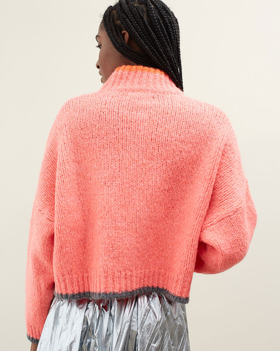 back view of model wearing slightly cropped coral cardigan with grey patch pockets and trim