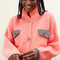 up close of model wearing slightly cropped coral cardigan with grey patch pockets and trim