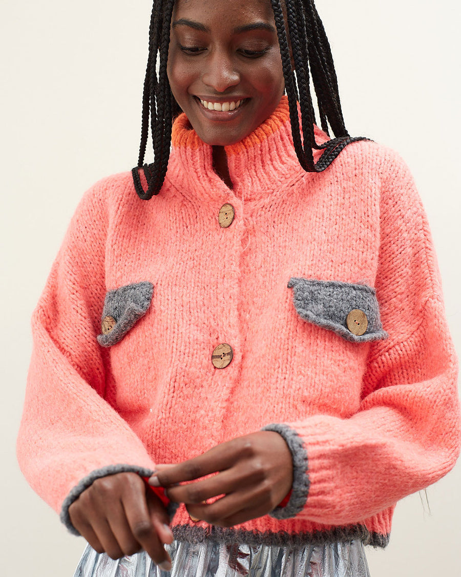 up close of model wearing slightly cropped coral cardigan with grey patch pockets and trim