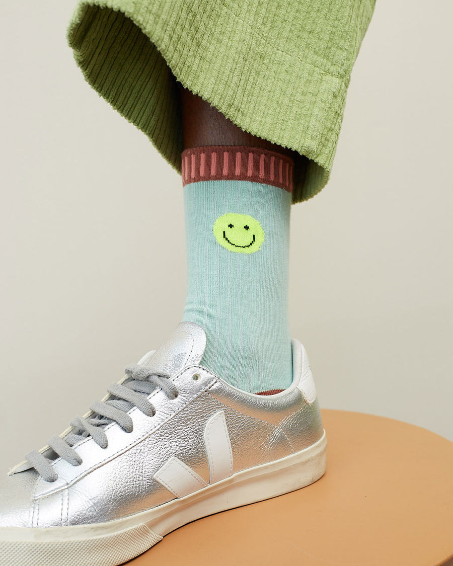 up close of model wearing blue socks with neon smiley on the cuff