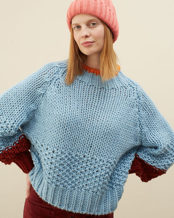 model wearing light blue sweater with maroon cuffs and orange neckline