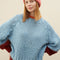 model wearing light blue sweater with maroon cuffs and orange neckline