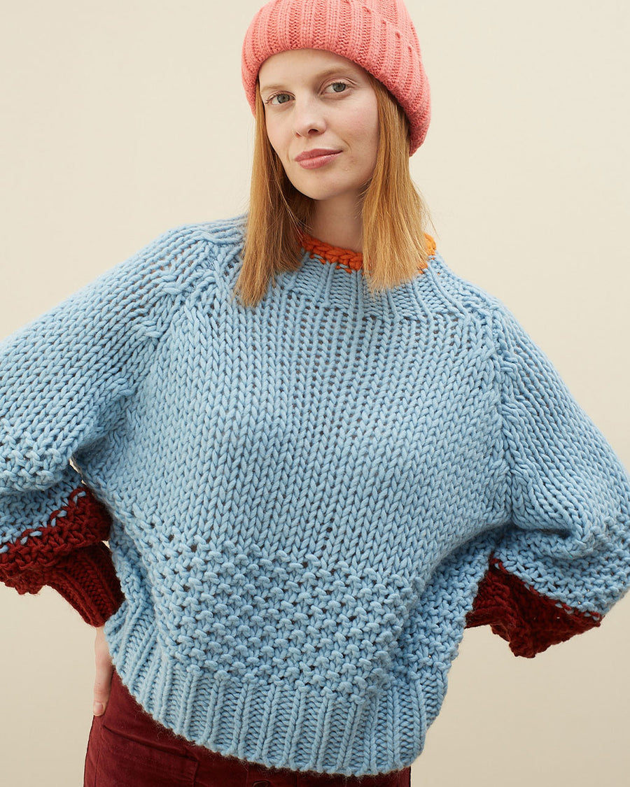 model wearing light blue sweater with maroon cuffs and orange neckline