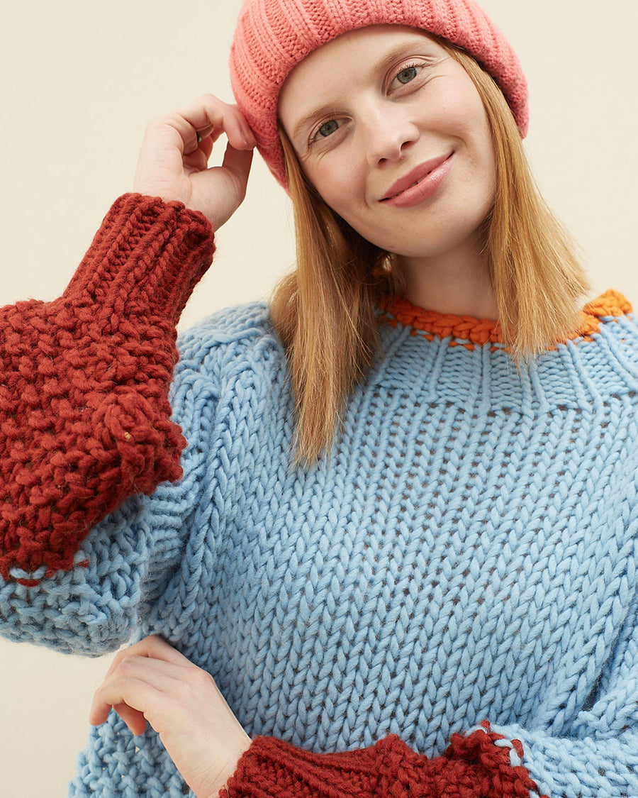 up close of model wearing light blue sweater with maroon cuffs and orange neckline