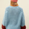 back view of model wearing light blue sweater with maroon cuffs and orange neckline