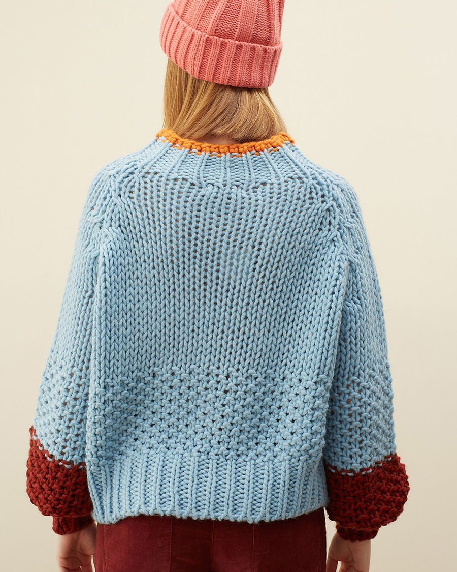 back view of model wearing light blue sweater with maroon cuffs and orange neckline