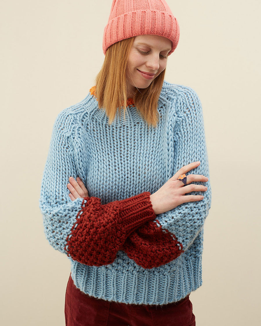 model wearing light blue sweater with maroon cuffs and orange neckline