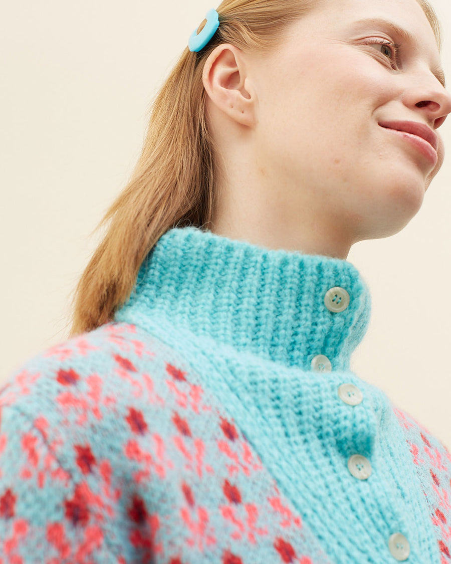 up close of model wearing blue sweater with button funnel neckline and pink abstract floral print