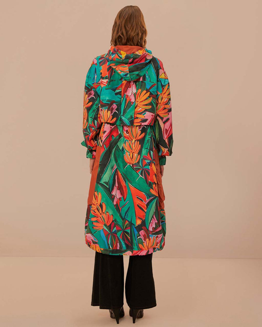 back view of model wearing teal long raincoat with colorful palm print, cargo pocket, and hood