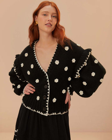 model wearing black cardigan with 3D white floral print, and ruffles on the the sleeves