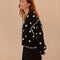 side view of model wearing black cardigan with 3D white floral print, and ruffles on the the sleeves