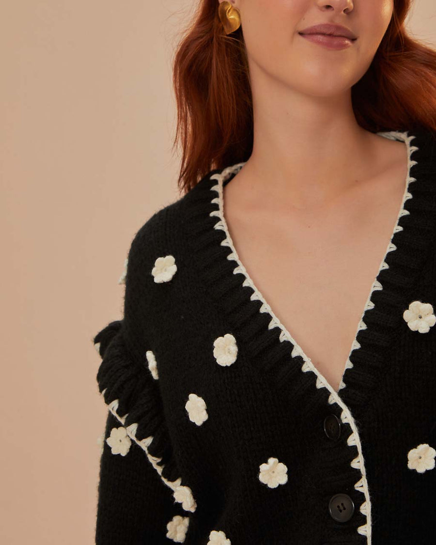 up close of model wearing black cardigan with 3D white floral print, and ruffles on the the sleeves