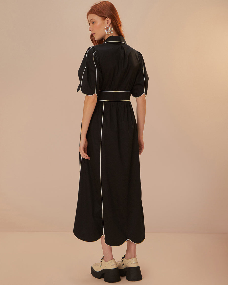 back view of model wearing black cotton midi dress with scallop hem and white piping