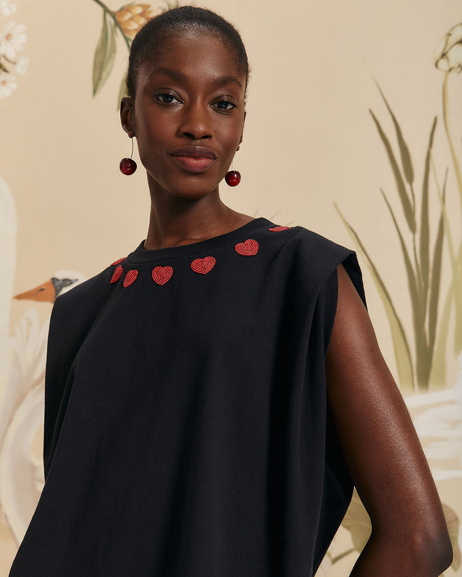 model wearing black cap sleeve top with red beaded heart shapes around the neckline