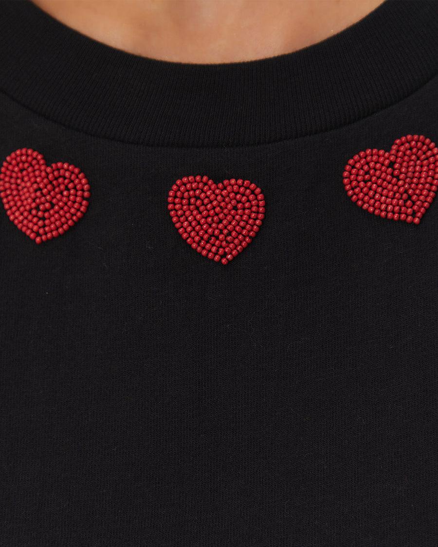 up close of model wearing black cap sleeve top with red beaded heart shapes around the neckline