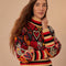 up close of model black sweater with colorful abstract hearts and striped mock neck, sleeve cuffs and hem