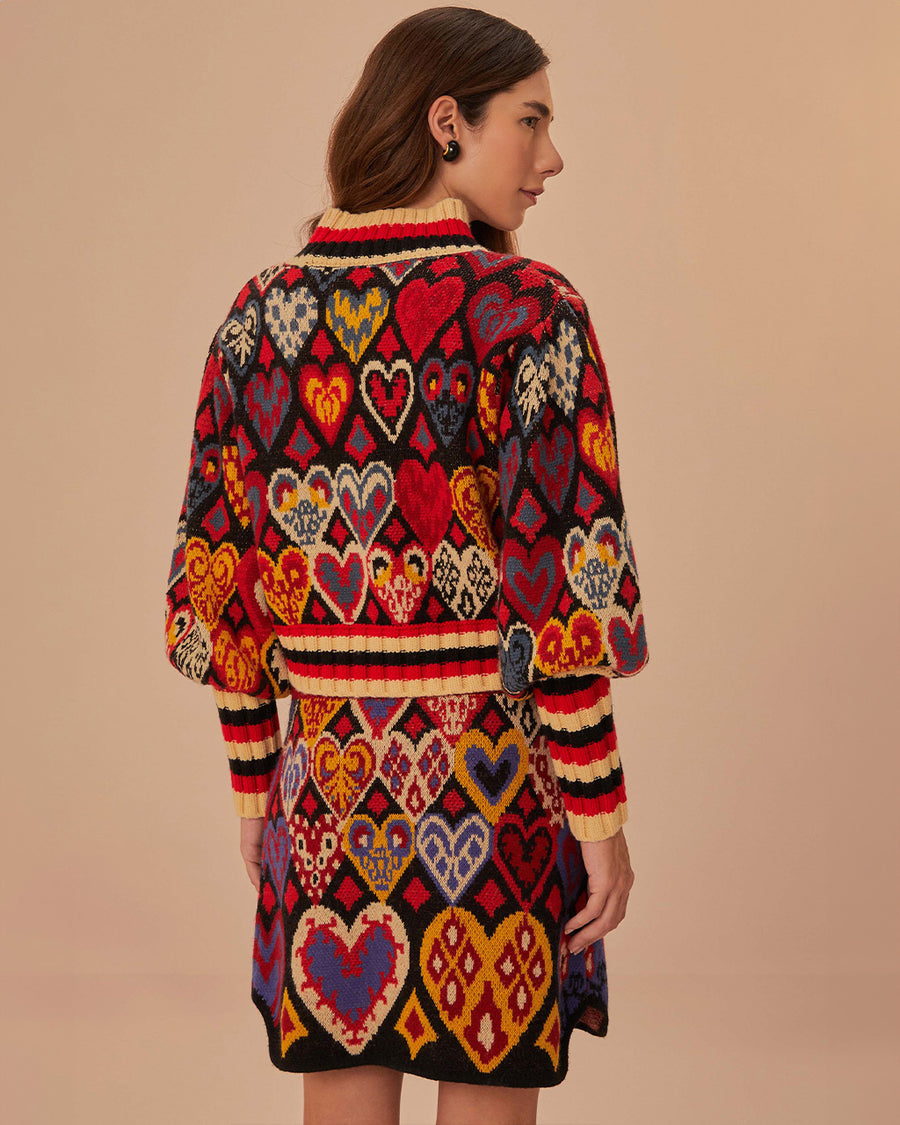 back view of model black sweater with colorful abstract hearts and striped mock neck, sleeve cuffs and hem