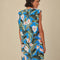 back view of model wearing blue mini t-shirt dress with white anthurium flower print and tie waist