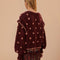 back view of model wearing brown cardigan with pink crochet flowers, ruffle on the sleeves and slight boxy cropped fit