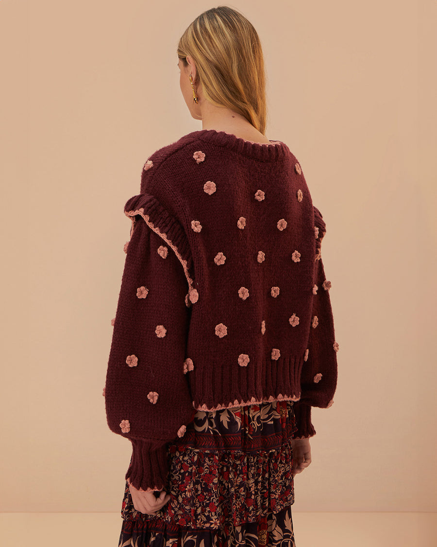 back view of model wearing brown cardigan with pink crochet flowers, ruffle on the sleeves and slight boxy cropped fit