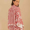 back view of model wearing cropped white and red stripe button down top with flared sleeves and floral and chain charm print