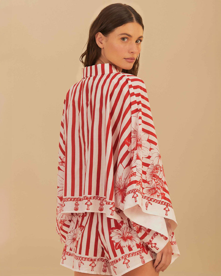 back view of model wearing cropped white and red stripe button down top with flared sleeves and floral and chain charm print