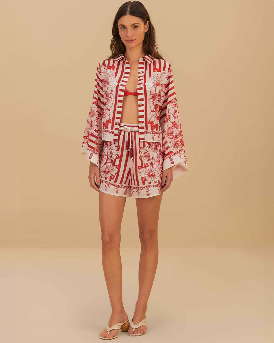 model wearing white and red stripe shorts with beaded tie waist tassels, dolphin hem sides and floral and chain charm print