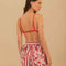 back view of model wearing white and red stripe shorts with beaded tie waist tassels, dolphin hem sides and floral and chain charm print