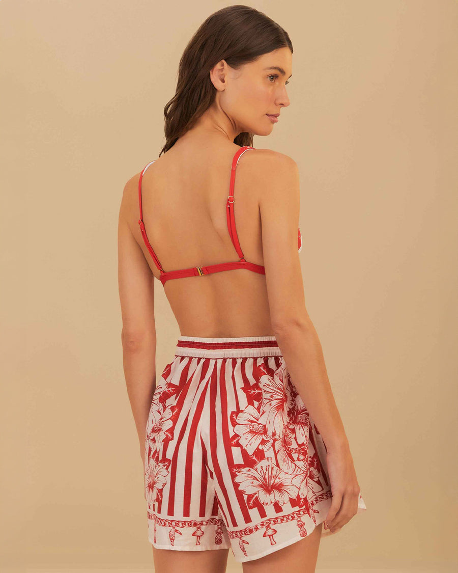 back view of model wearing white and red stripe shorts with beaded tie waist tassels, dolphin hem sides and floral and chain charm print