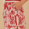 side view of model wearing white and red stripe shorts with beaded tie waist tassels, dolphin hem sides and floral and chain charm print