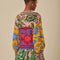 back view of model wearing colorful bird print cardigan with ric rac detail on the arms and bodice and striped trim