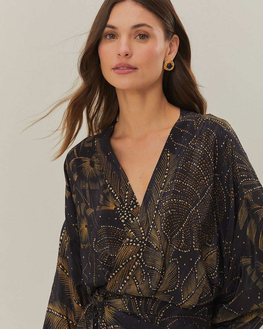 up close of model wearing black mini dress with tie waist, long sleeves and golden foliage print