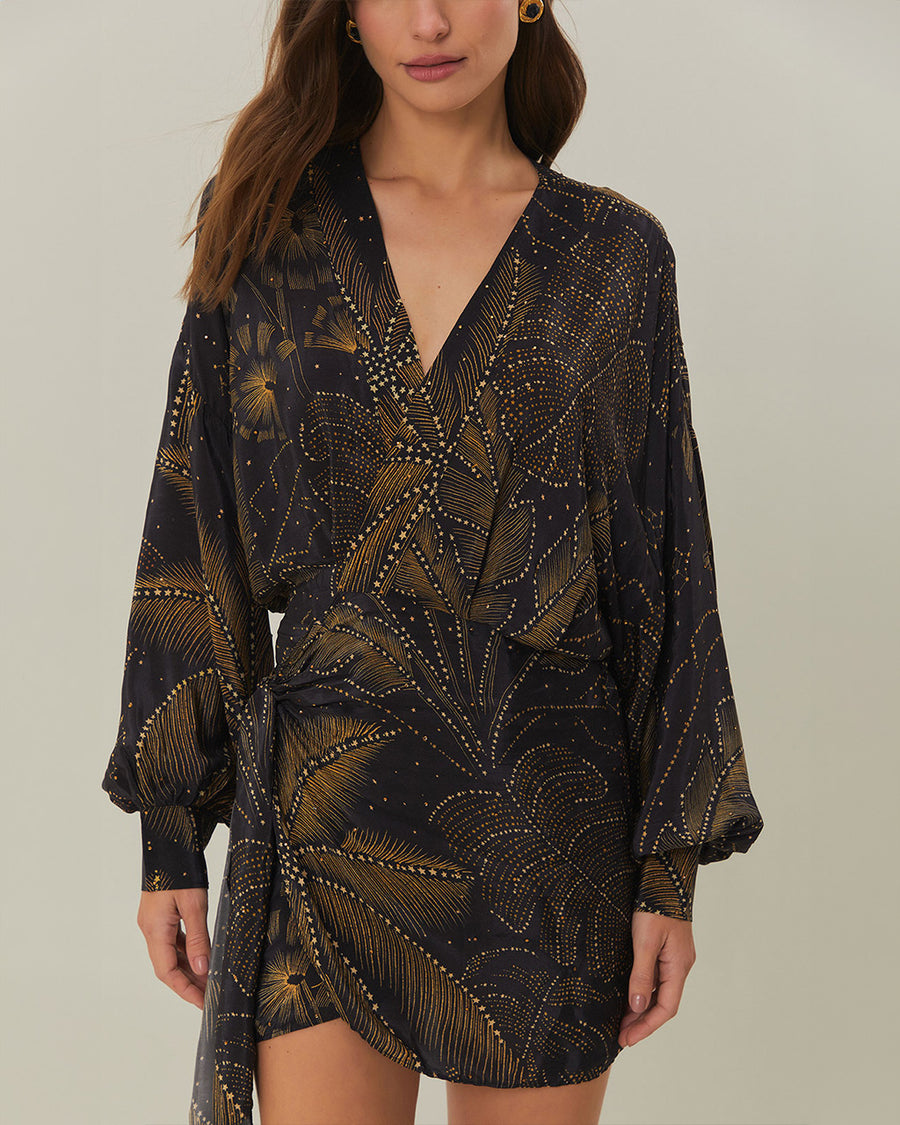 model wearing black mini dress with tie waist, long sleeves and golden foliage print