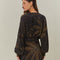 back view of model wearing black mini dress with tie waist, long sleeves and golden foliage print