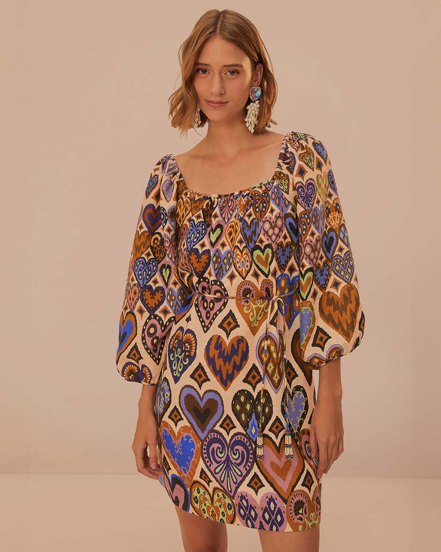 model wearing square neck mini dress with sand ground and colorful ikat heart print and long puff sleeves