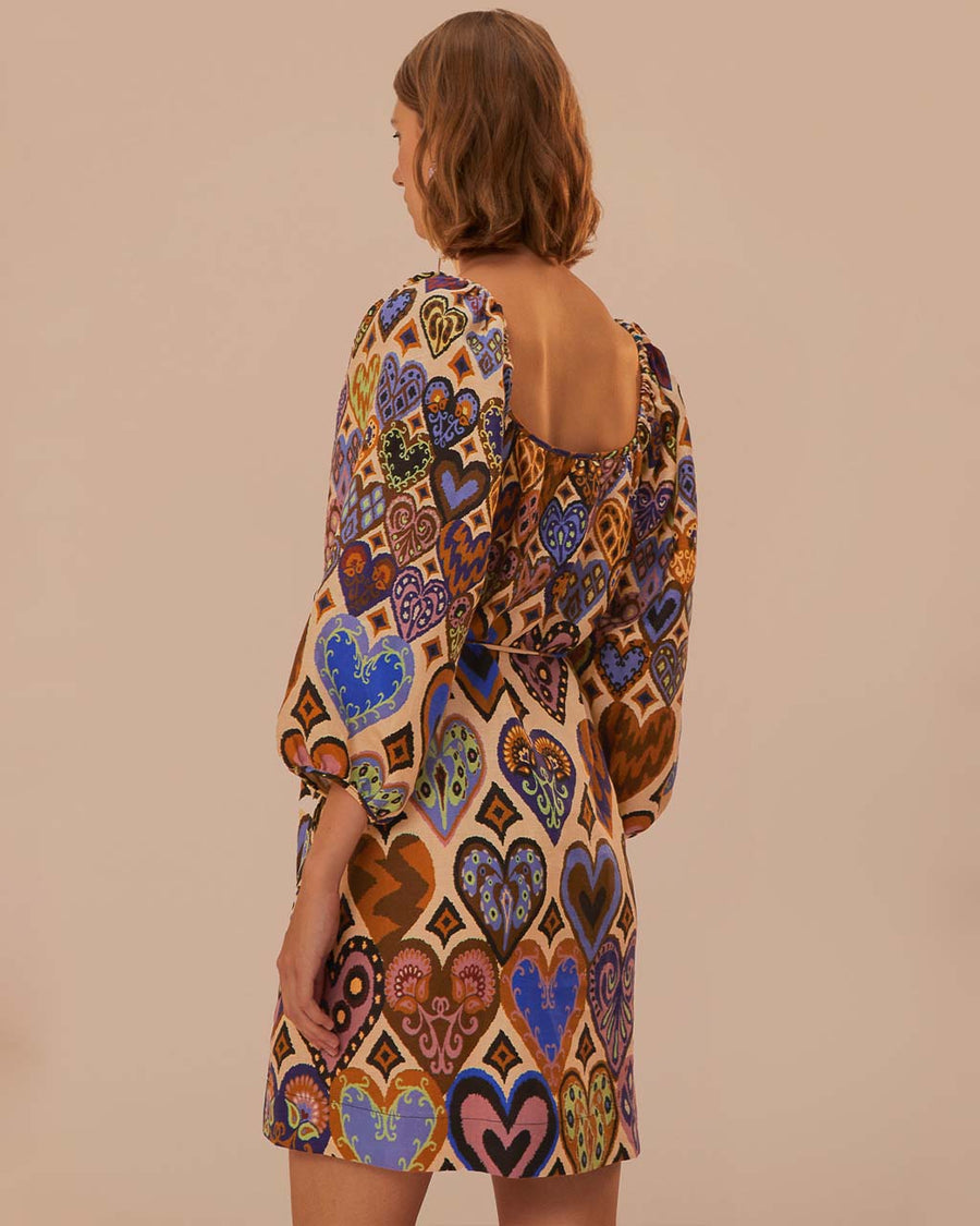 back view of model wearing square neck mini dress with sand ground and colorful ikat heart print and long puff sleeves