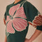 side view of model wearing green short sleeve sweater with burnt rust and pink flower print