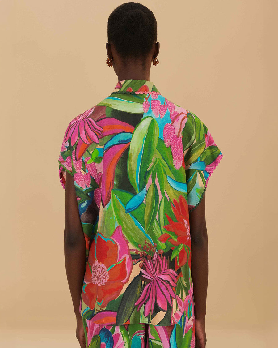 back view of model wearing colorful tropical floral print with button front and pink and green mini tassel detail on the placket and sleeves