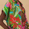 side view of model wearing colorful tropical floral print with button front and pink and green mini tassel detail on the placket and sleeves