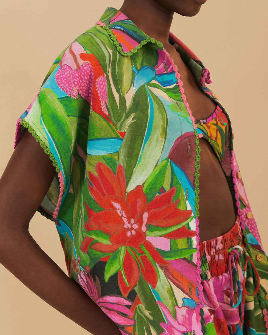 side view of model wearing colorful tropical floral print with button front and pink and green mini tassel detail on the placket and sleeves