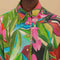 model wearing buttoned colorful tropical floral print with button front and pink and green mini tassel detail on the placket and sleeves