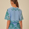 back view of model wearing. light blue cropped top with green cut out design and flutter sleeves