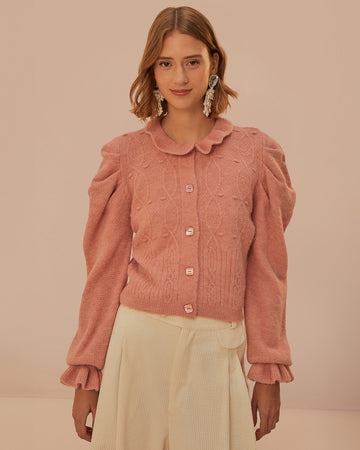 model wearing light pink cardigan with button front, ruched sleeves with ruffle detail and slight scalloped collar