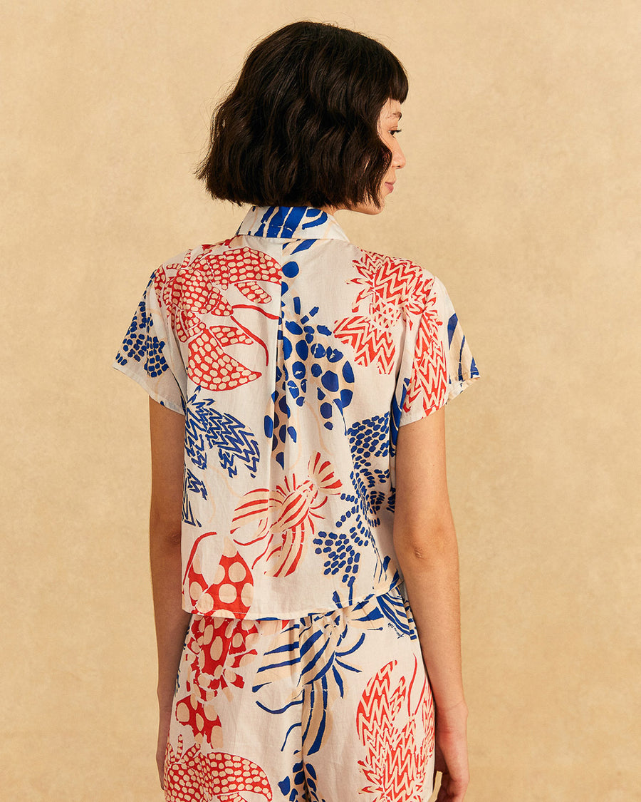 backview of model wearing off white short sleeve button down top with blue and red abstract lobster print