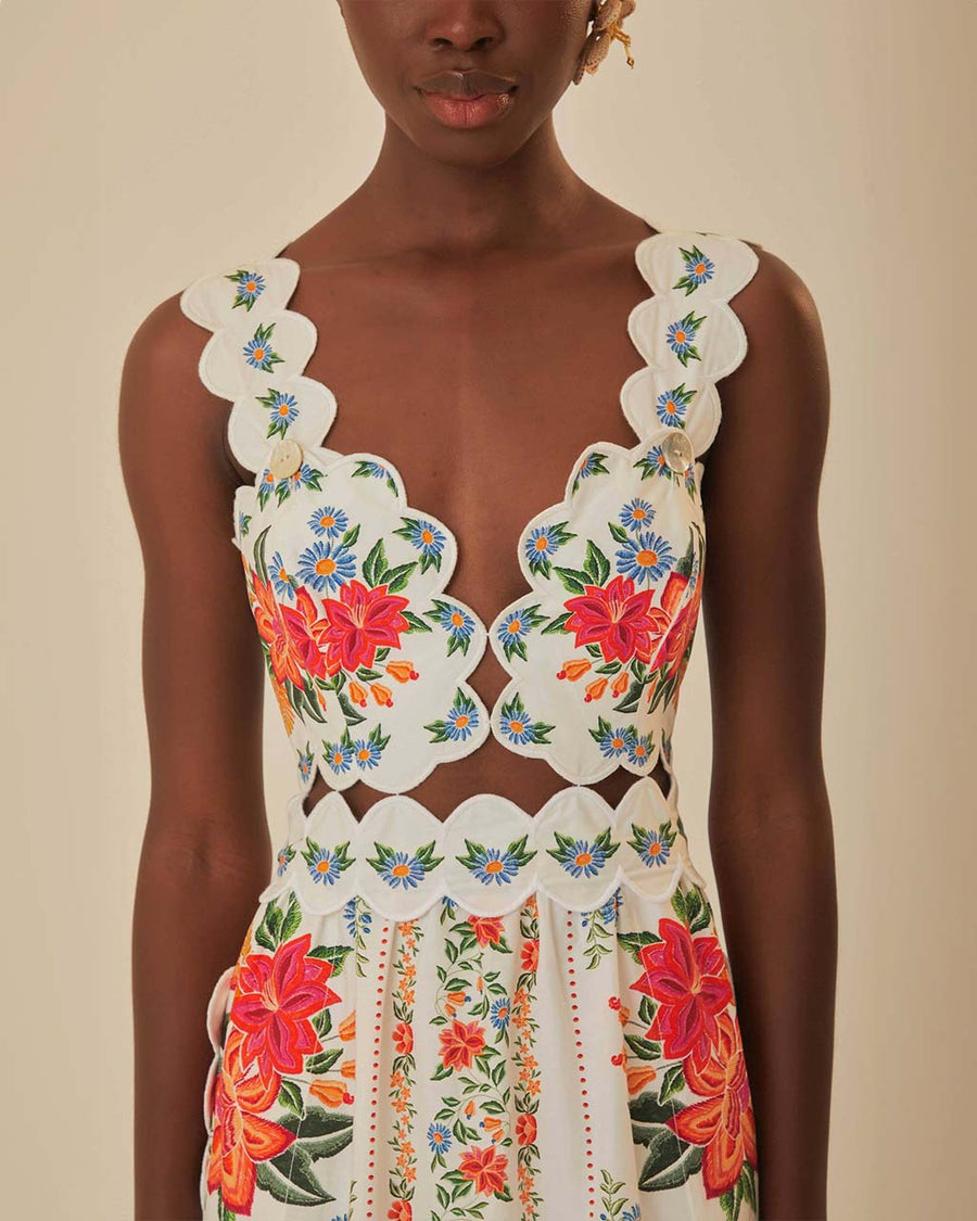 up close of  model wearing white midi dress with scalloped bodice and straps , cut out waist, and all over colorful floral print